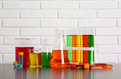 Different glassware with samples on table near brick wall. Solution chemistry