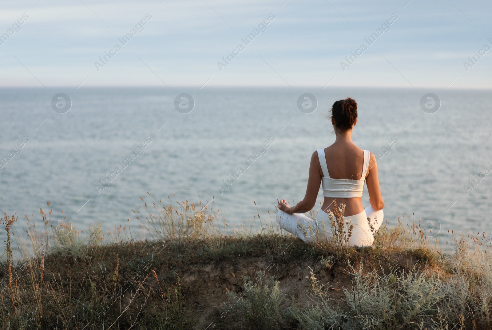 Photo of Woman meditating near sea, back view. Space for text