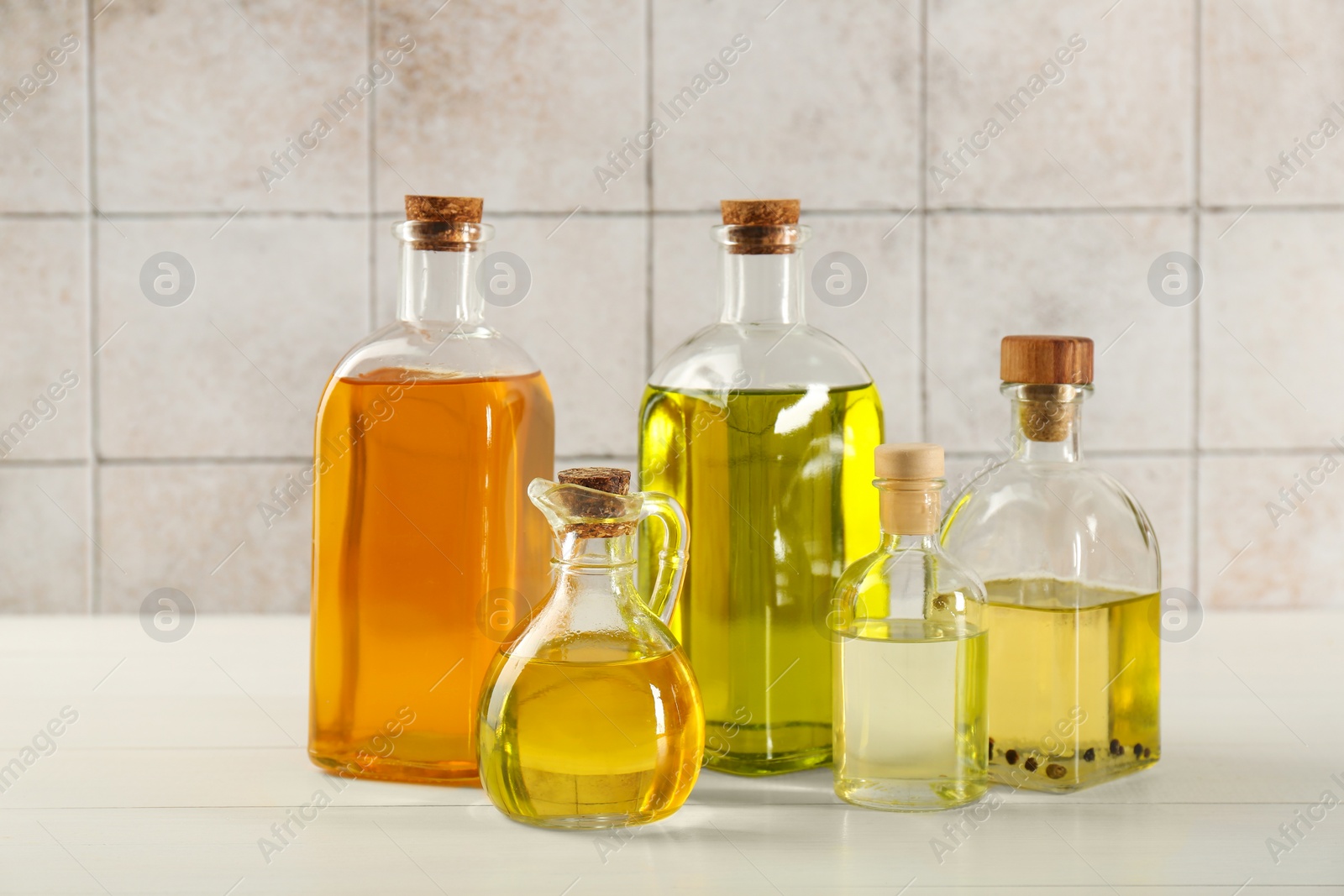Photo of Vegetable fats. Different oils in glass bottles on white wooden table against tiled wall
