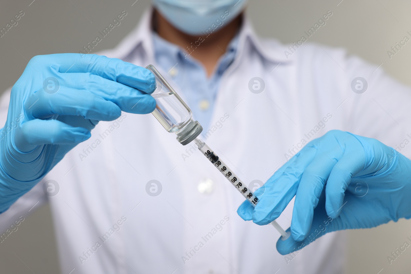 Photo of Doctor filling syringe with medication from glass vial on grey background, closeup