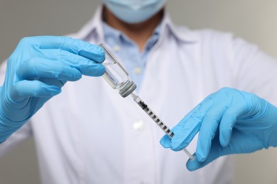 Doctor filling syringe with medication from glass vial on grey background, closeup