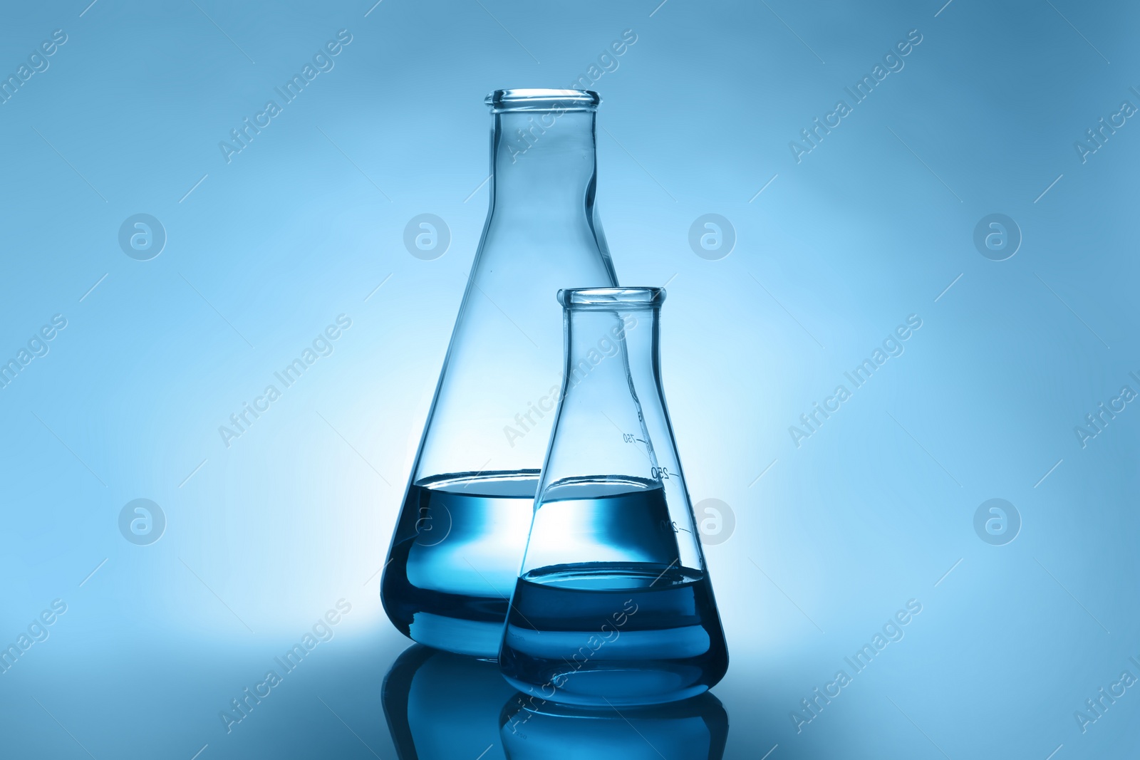 Photo of Conical flasks with liquid on table against color background. Laboratory analysis