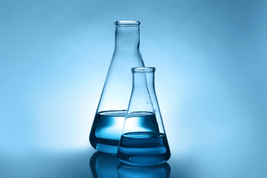 Conical flasks with liquid on table against color background. Laboratory analysis