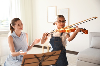 Photo of Young woman teaching little girl to play violin indoors