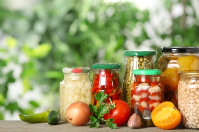 Fresh vegetables and jars of pickled products on wooden table