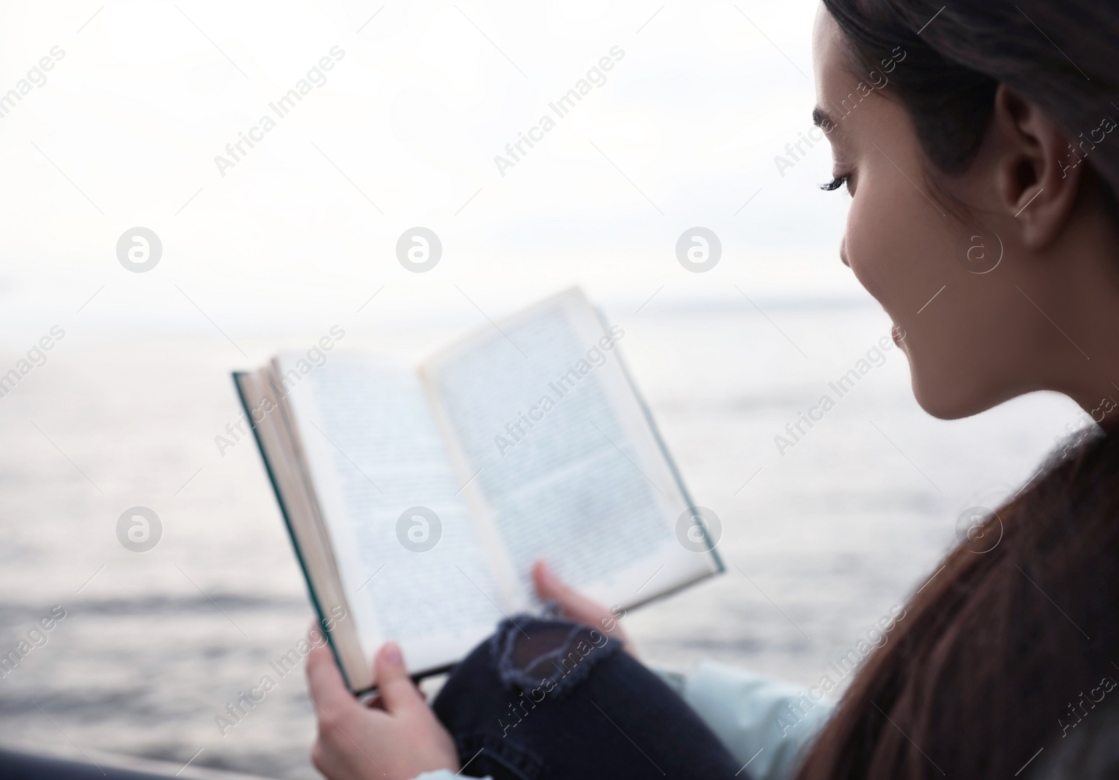 Photo of Woman reading book near river on cloudy day