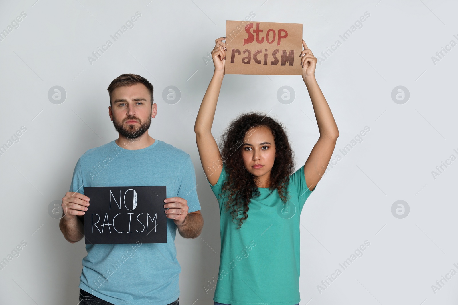 Photo of Young man and African American woman holding signs on grey background. Racism concept
