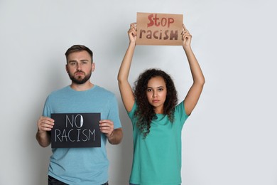 Young man and African American woman holding signs on grey background. Racism concept