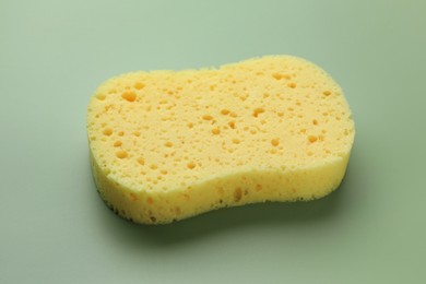 Photo of New yellow sponge on green background, closeup
