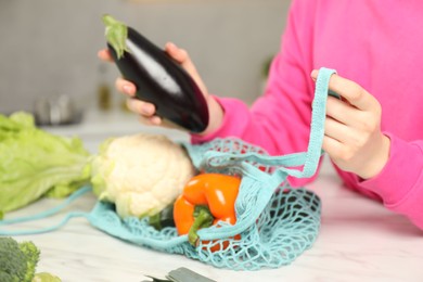 Woman taking eggplant out from string bag at light marble table, closeup