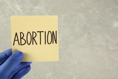 Photo of Doctor holding paper card with word ABORTION on light grey background, closeup. Space for text