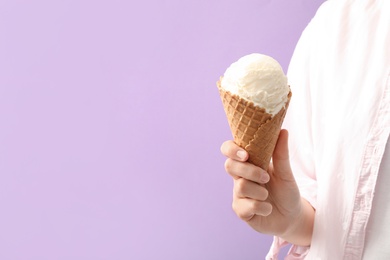 Woman holding white ice cream in wafer cone on violet background, closeup. Space for text