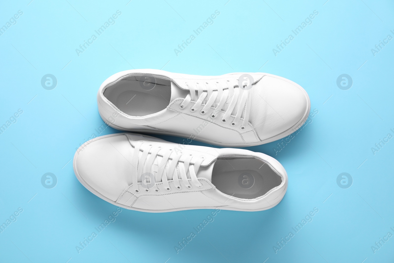 Photo of Pair of stylish white sneakers on light blue background, top view