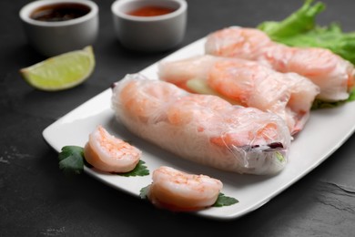 Delicious spring rolls with shrimps wrapped in rice paper served on black table, closeup