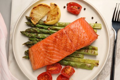 Photo of Tasty grilled salmon with asparagus, tomatoes, spices and lemon served on light grey table, top view