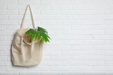 Photo of Eco tote bag with leaf hanging on white brick wall. Space for text