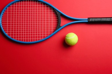 Tennis racket and ball on red background, flat lay. Space for text