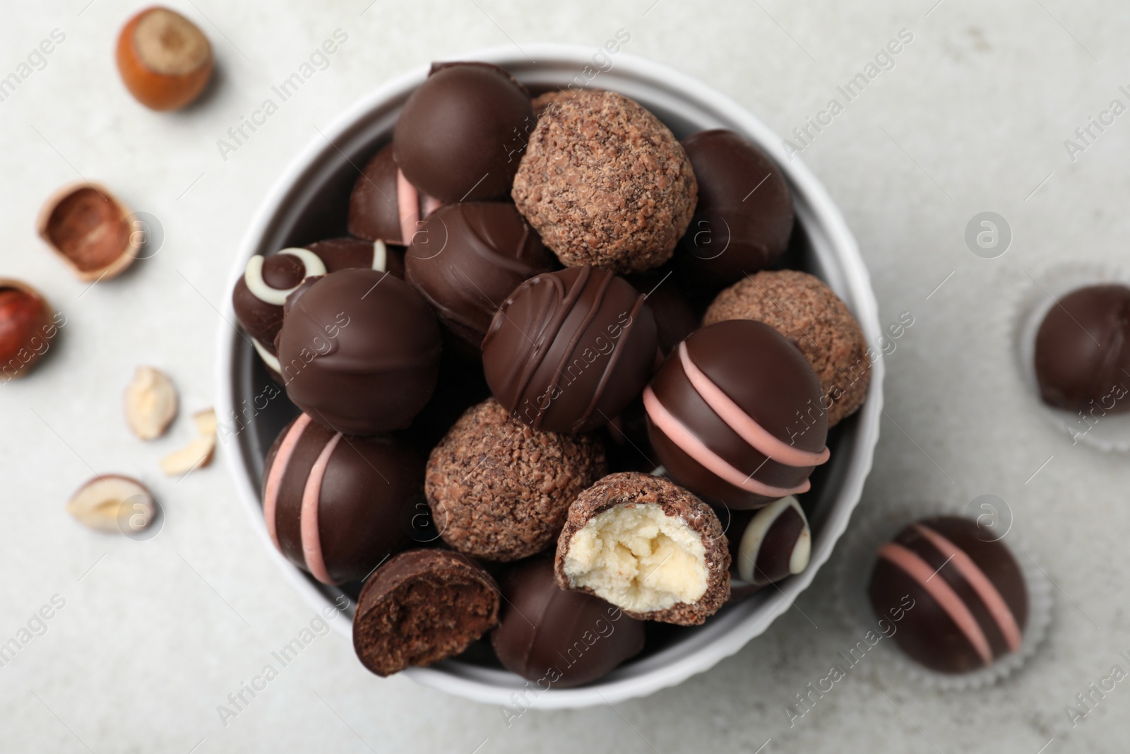 Photo of Different delicious chocolate truffles in bowl on light grey table, flat lay