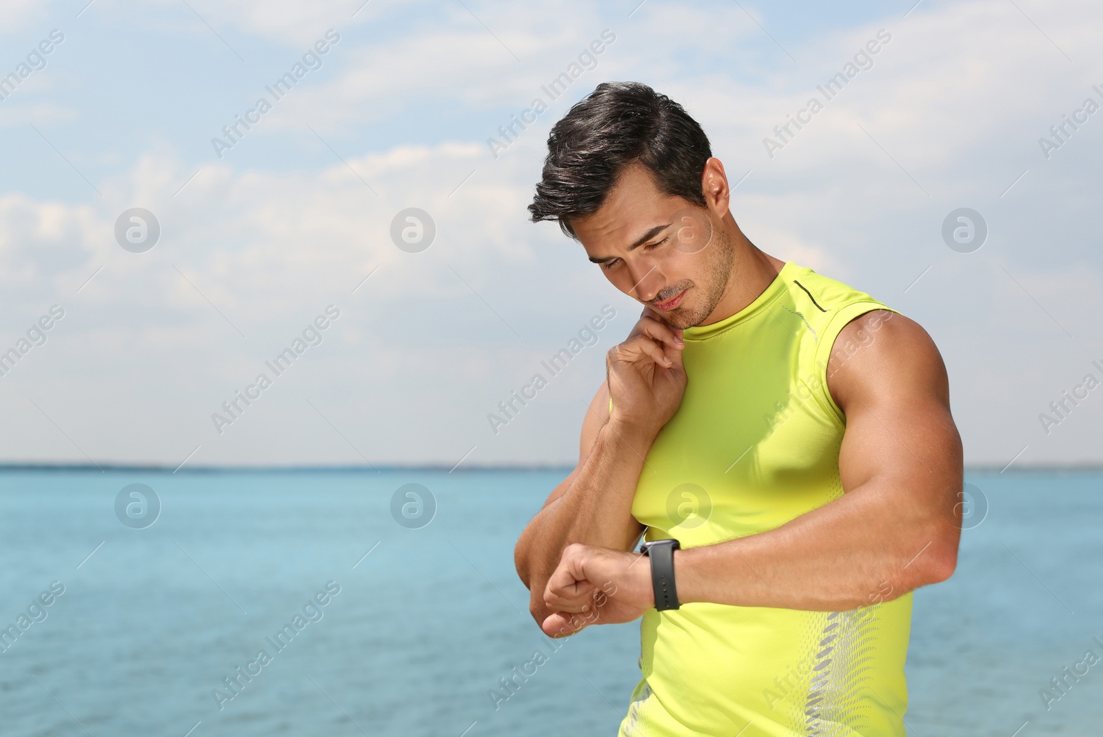 Photo of Young man checking pulse after training on beach. Space for text