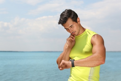 Photo of Young man checking pulse after training on beach. Space for text