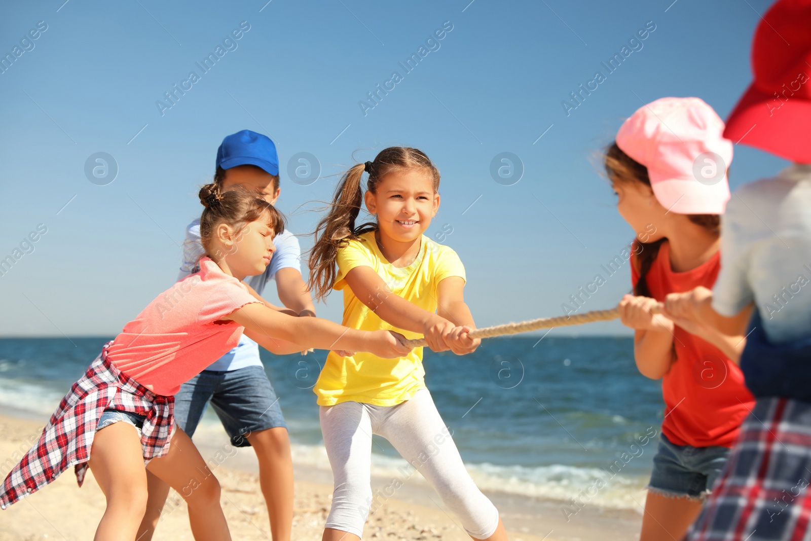 Photo of Cute children pulling rope during tug of war game on beach. Summer camp