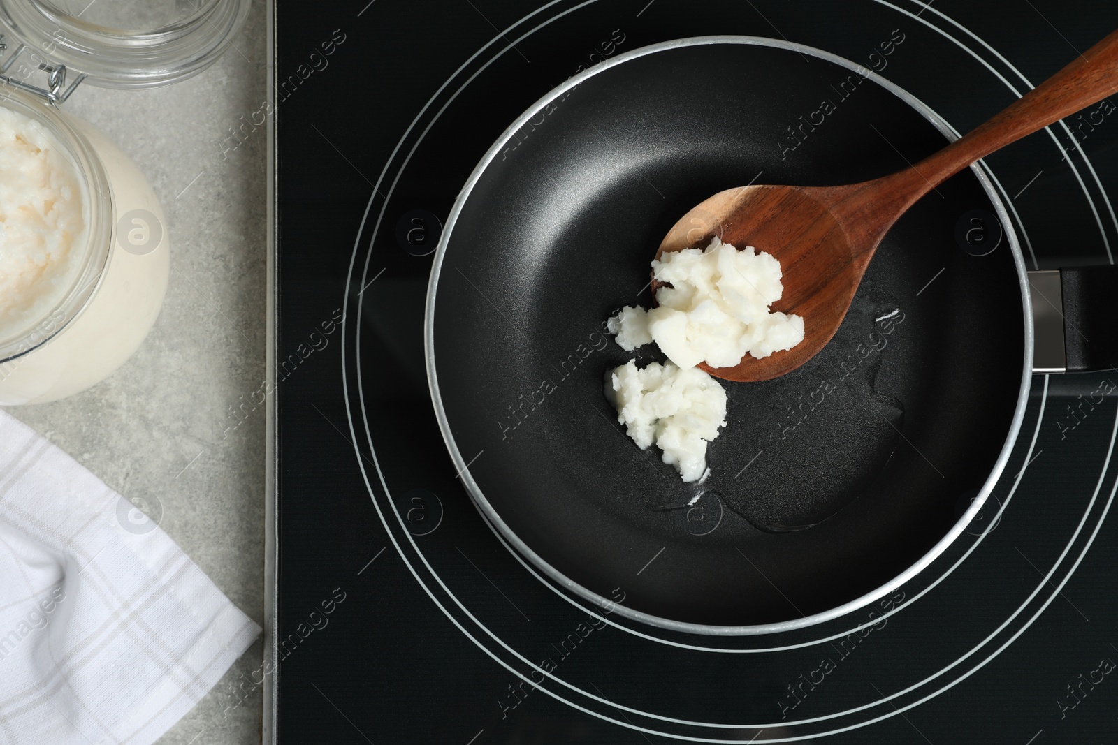 Photo of Frying pan with coconut oil and wooden spatula on induction stove, top view. Healthy cooking