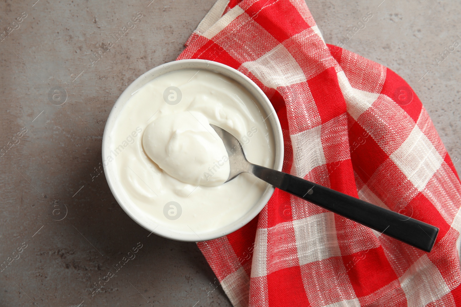 Photo of Bowl and spoon of fresh yogurt with napkin on grey background, flat lay