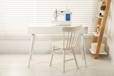 Photo of Sewing machine on white desk near chair indoors