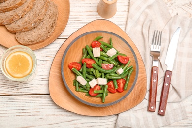 Photo of Plate with tasty green beans, tomatoes and cheese on wooden table, top view