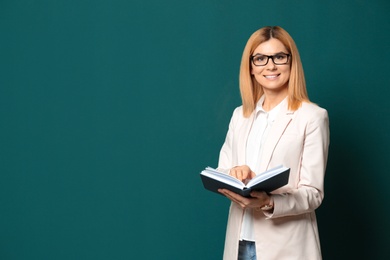 Portrait of beautiful teacher with book near chalkboard, space for text