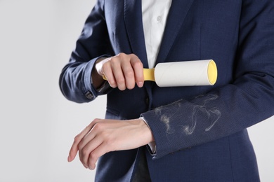 Photo of Woman removing cat hair from dark blue jacket with lint roller on grey background, closeup