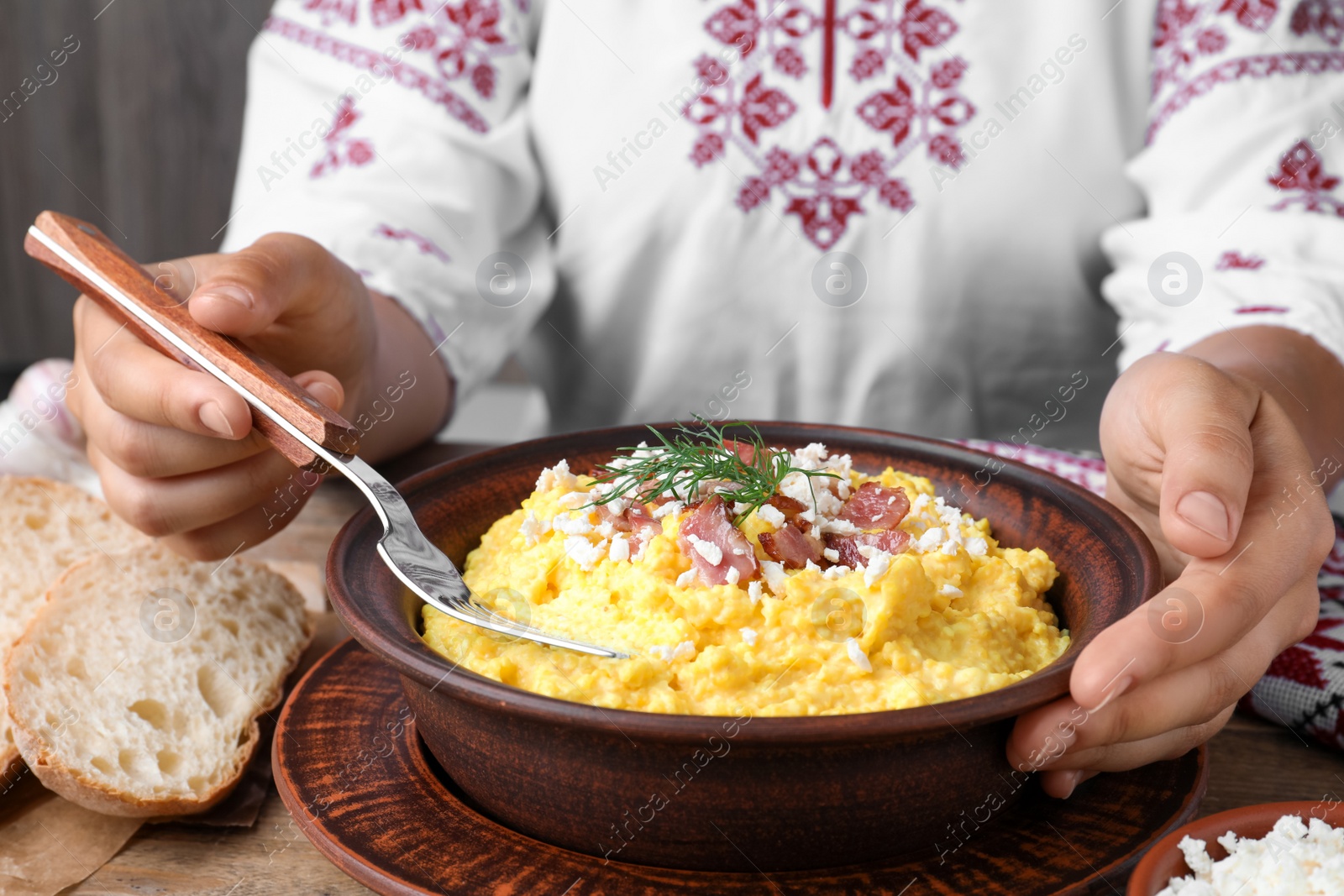 Photo of Woman eating banosh with brynza and pork cracklings at wooden table, closeup. Traditional Ukrainian dish