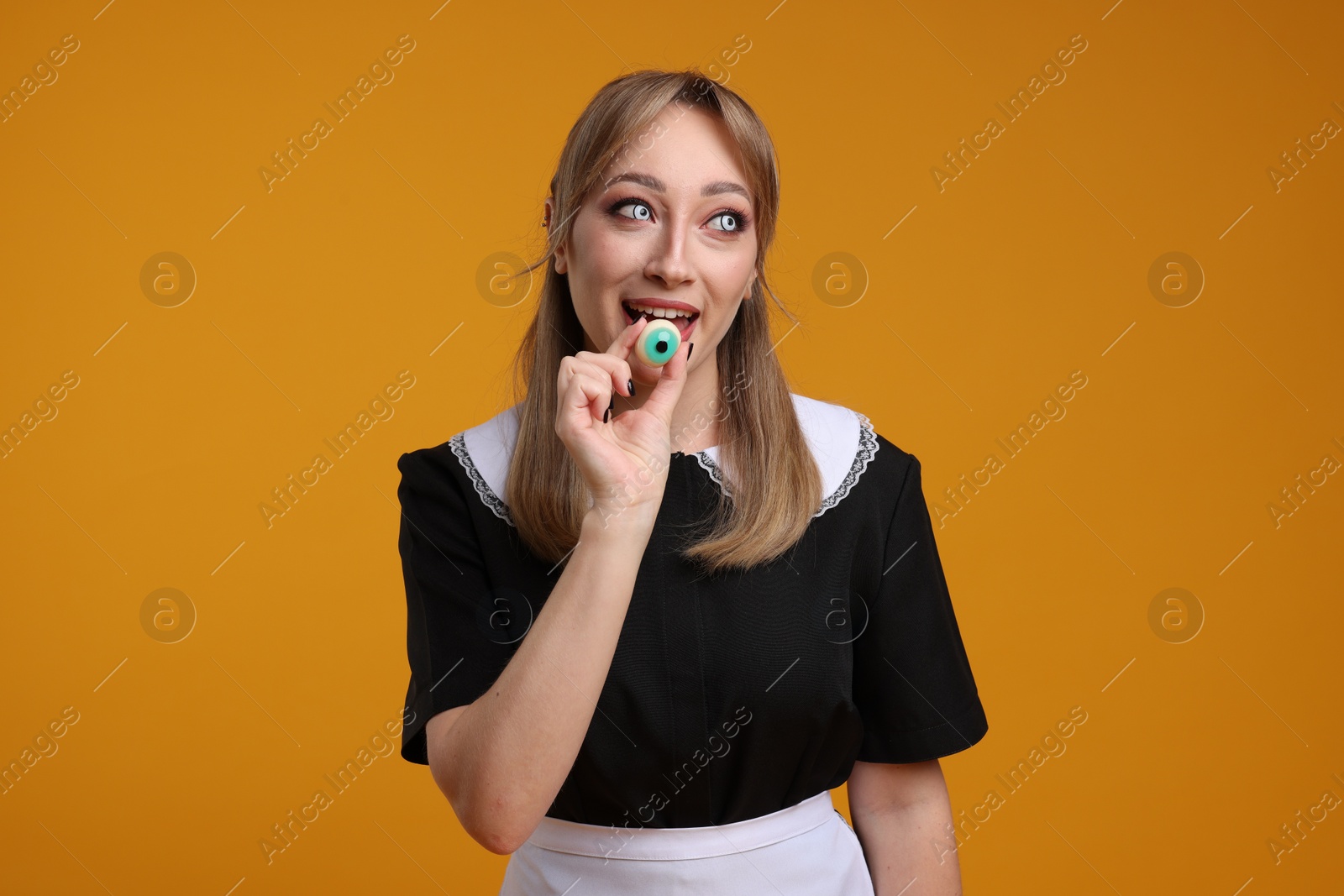 Photo of Happy woman in scary maid costume with decorative eyeball on orange background. Halloween celebration