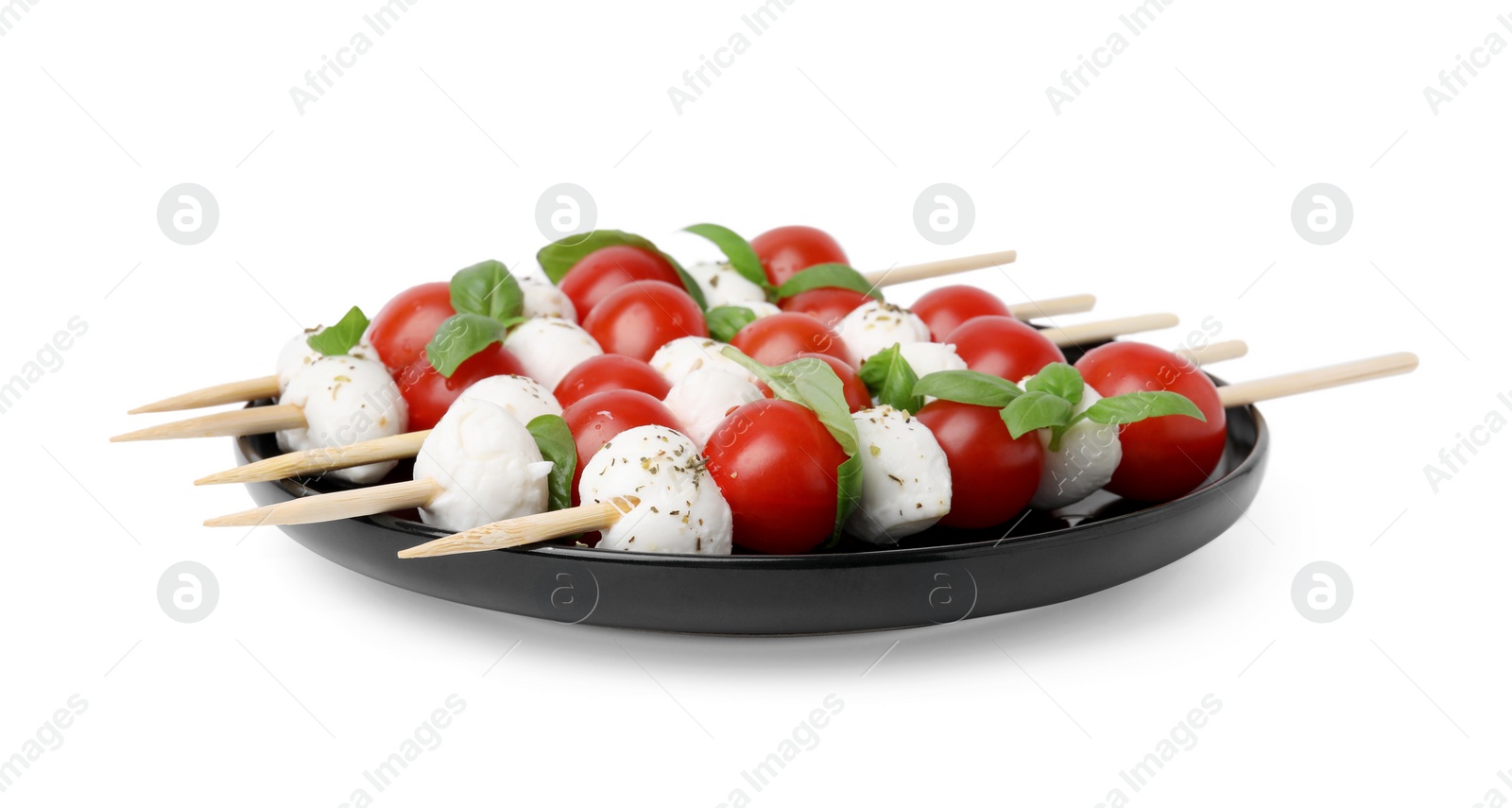 Photo of Plate of Caprese skewers with tomatoes, mozzarella balls, basil and spices isolated on white