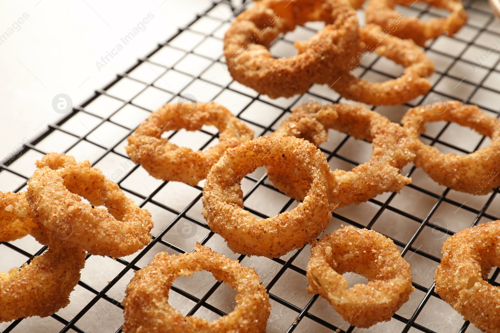 Photo of Cooling rack with homemade crunchy fried onion rings on table, closeup