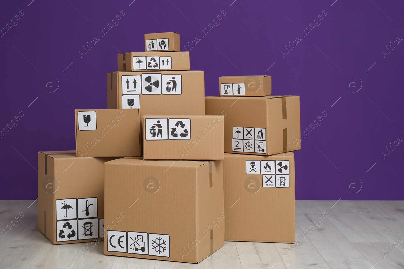 Photo of Cardboard boxes with different packaging symbols on floor near purple wall. Parcel delivery