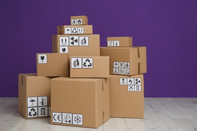 Cardboard boxes with different packaging symbols on floor near purple wall. Parcel delivery