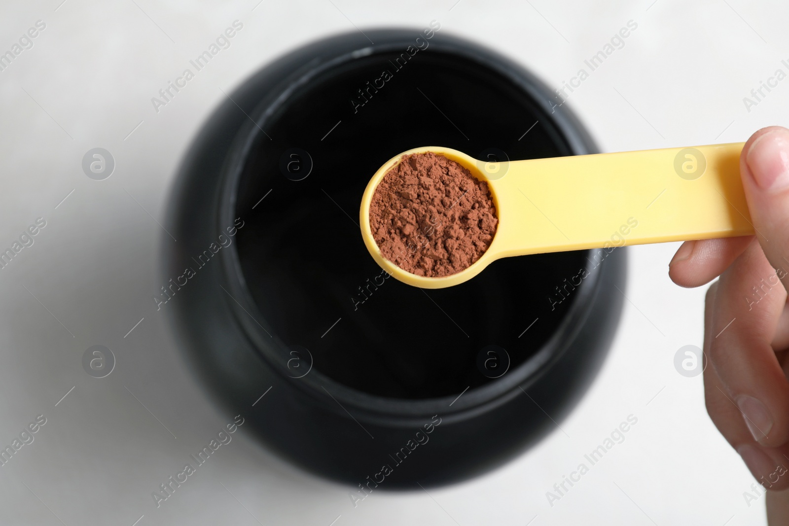 Photo of Man holding scoop of protein powder over jar on light background, top view