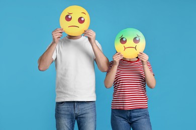 People covering faces with emoticons on light blue background