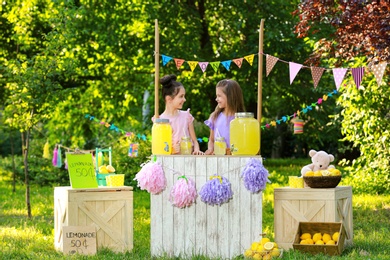 Photo of Cute little girls at lemonade stand in park. Summer refreshing natural drink