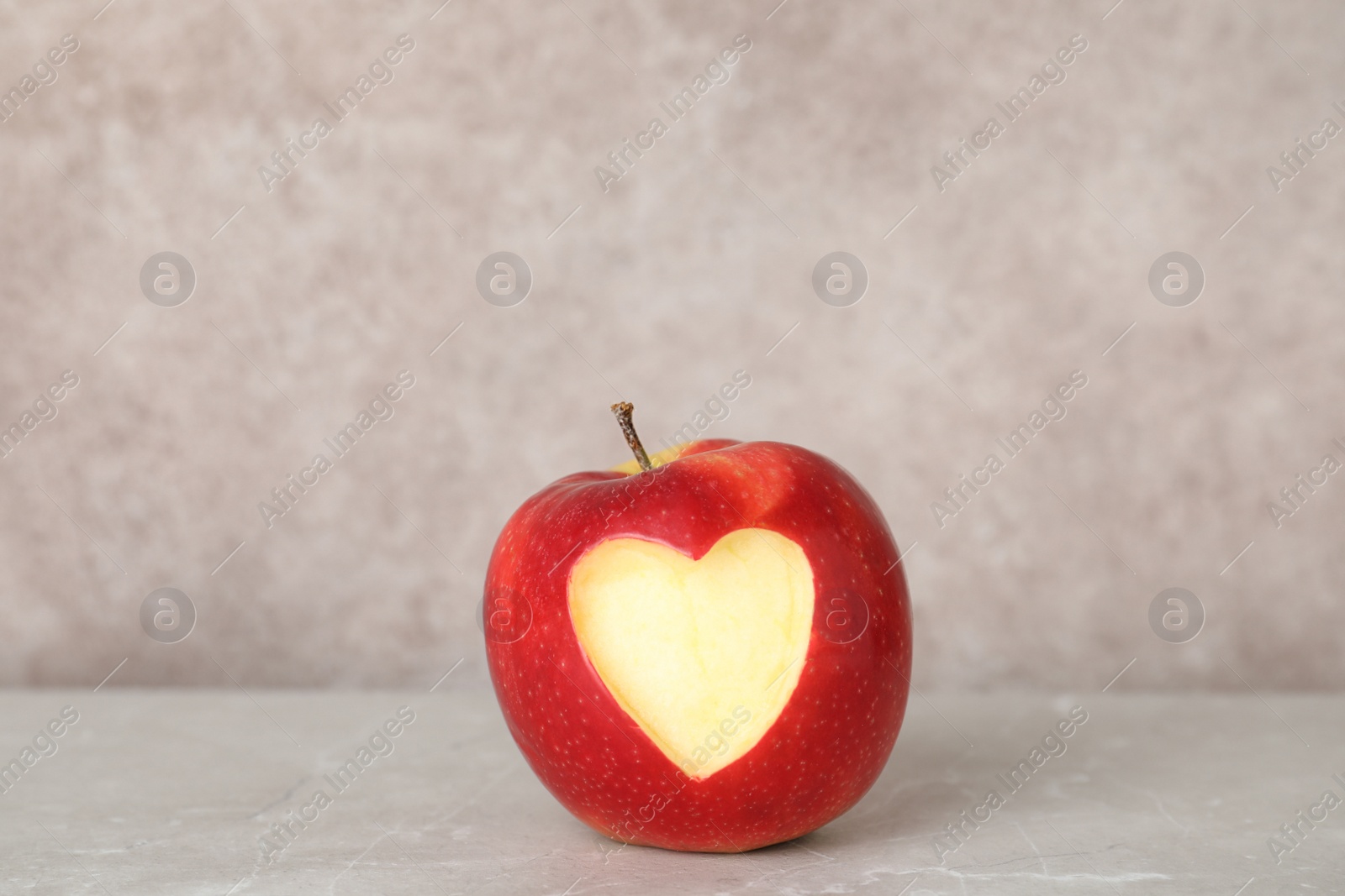 Photo of Red apple with carved heart on table against grey background