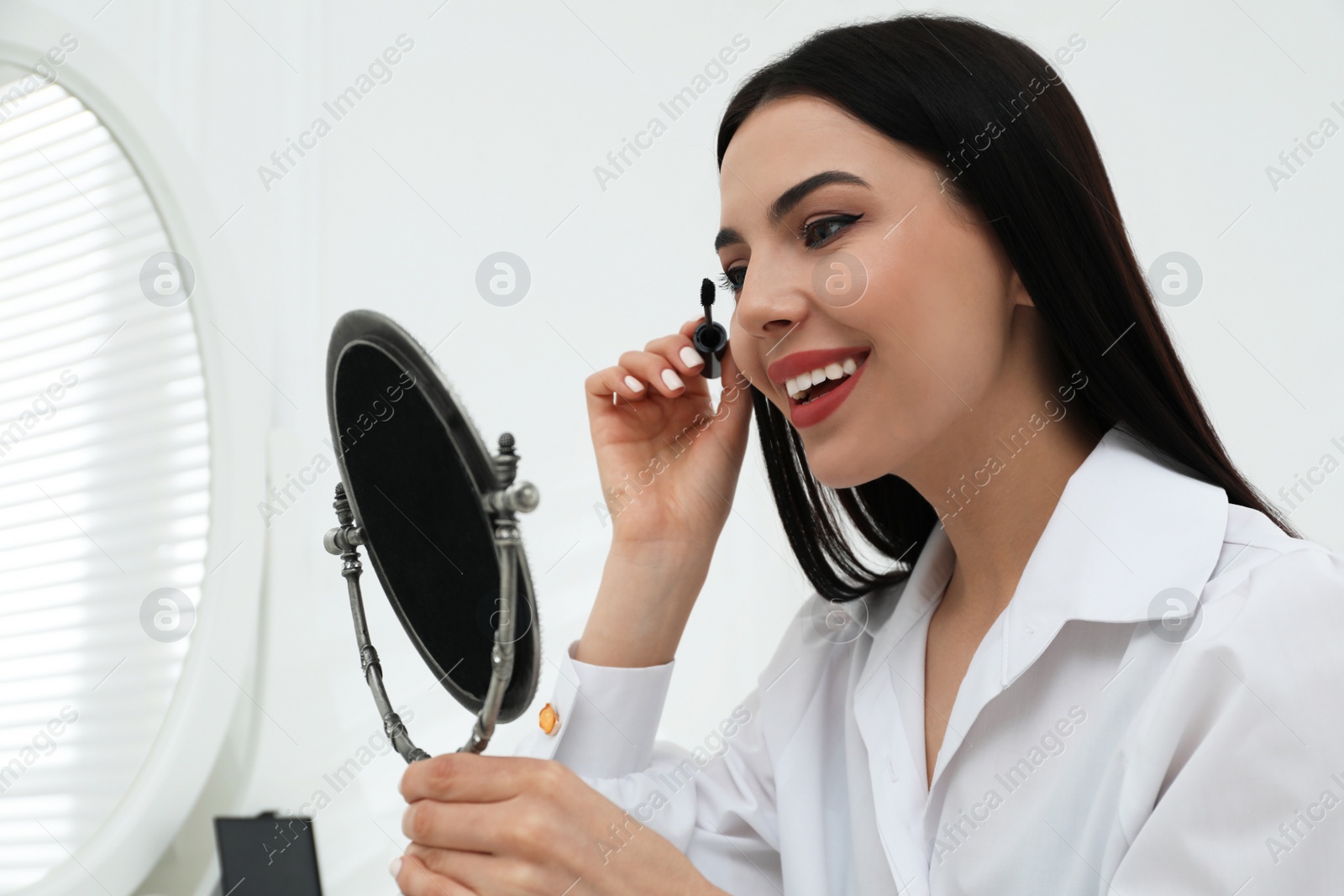 Photo of Beautiful woman applying makeup near mirror in room