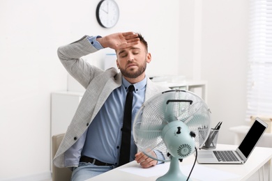 Man suffering from heat in front of fan at workplace