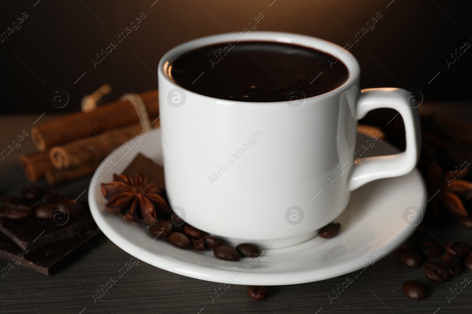 Photo of Cup of delicious hot chocolate, spices and coffee beans on wooden table