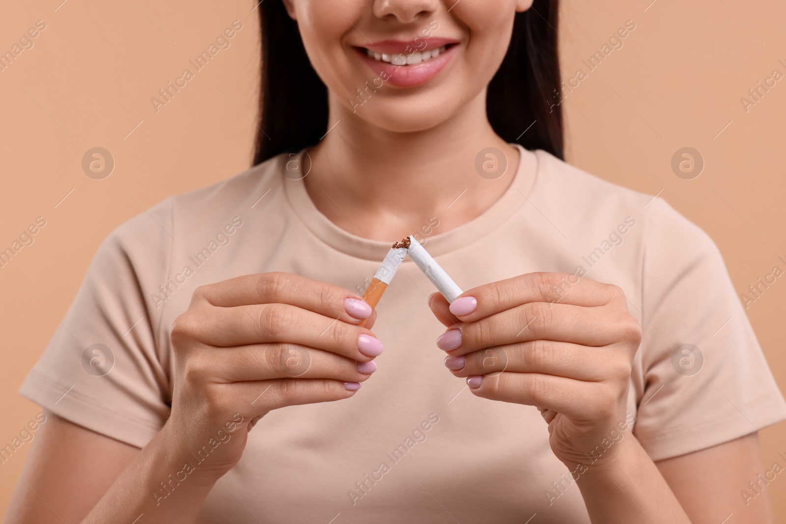 Photo of Stop smoking concept. Woman breaking cigarette on light brown background, closeup