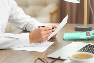 Man working with documents at wooden table in office, closeup