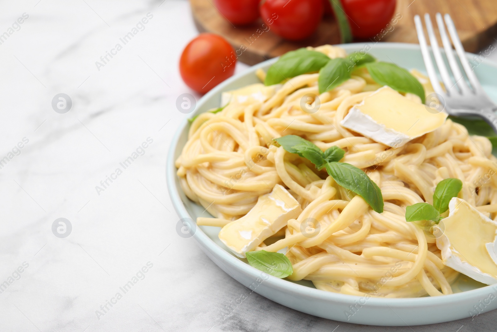 Photo of Delicious pasta with brie cheese and basil leaves on white marble table, closeup. Space for text