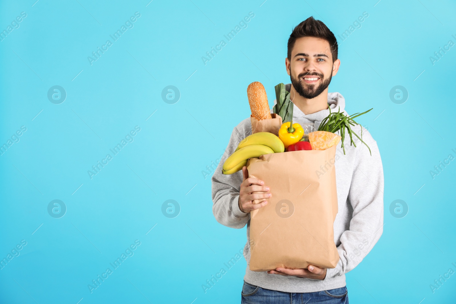 Photo of Man holding paper bag with fresh products on color background, space for text. Food delivery service