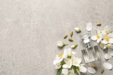 Photo of Bottle of luxury perfume and fresh jasmine flowers on light grey table, flat lay. Space for text