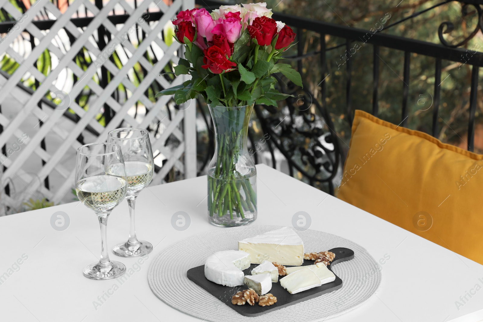 Photo of Beautiful roses, glasses of wine and snacks on white table at balcony